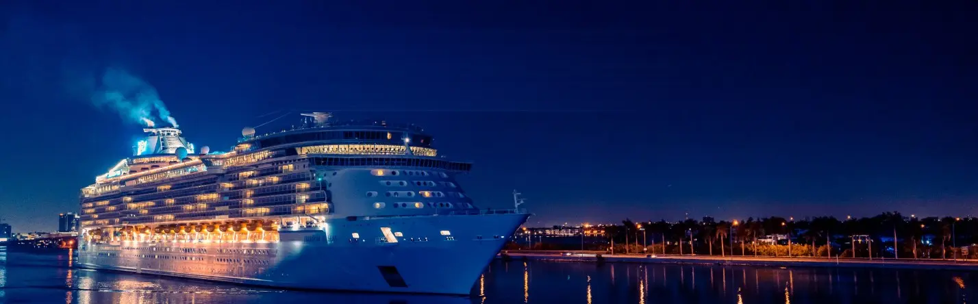A cruise ship lit up at night leaving port